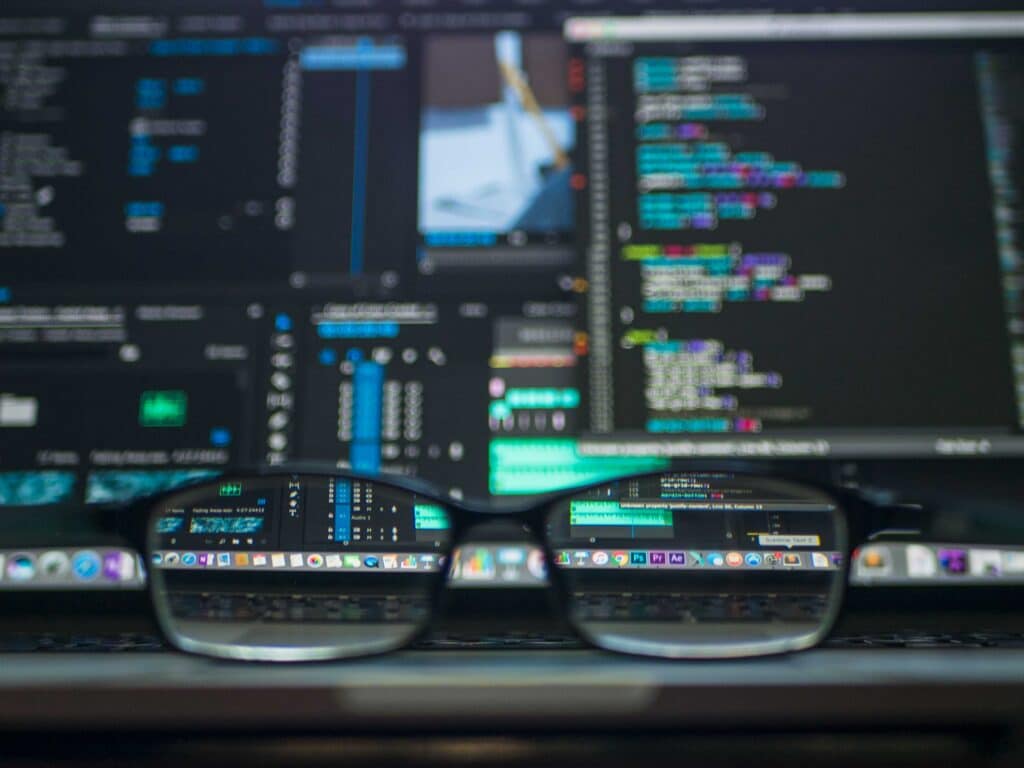glasses in front of computer screens with coding and alert symbolize cyber attacks