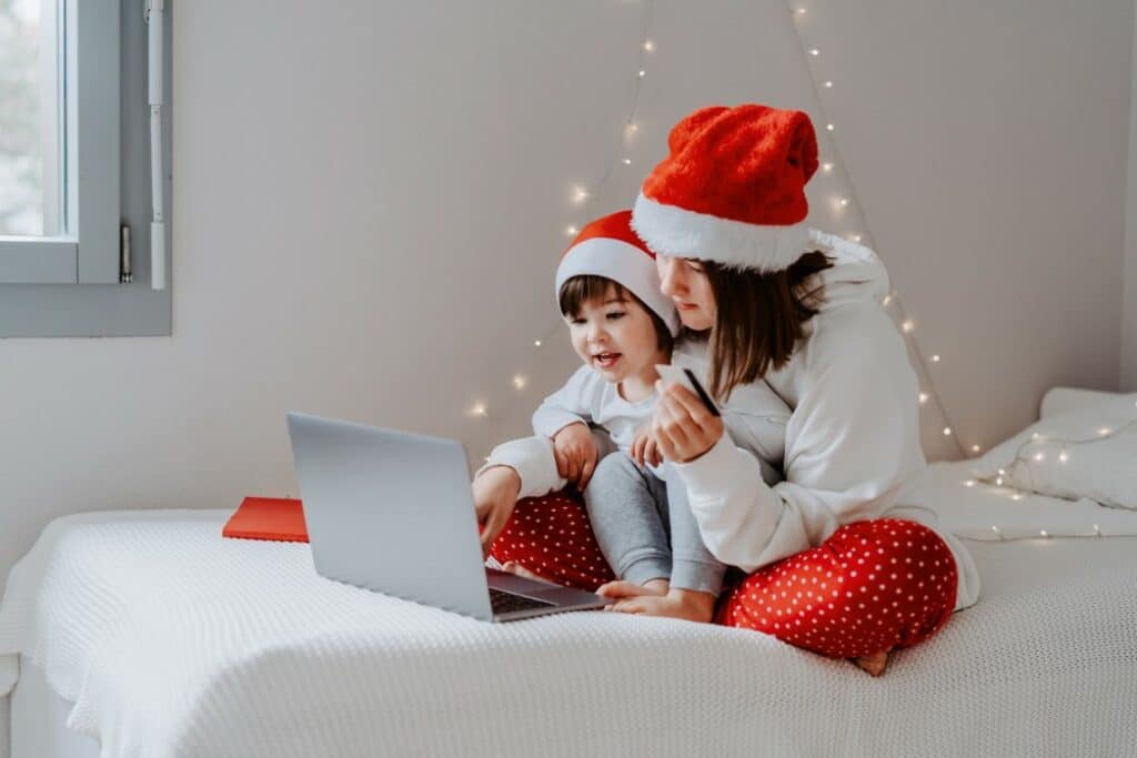 protect from holiday cyber crime - mother and child in santa hats use laptop on bed