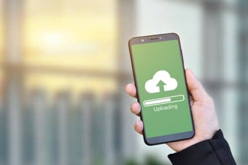 how to save on cloud spending - hand holding cell phone with cloud uploading symbol on green background